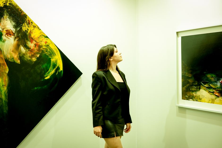 A woman in a black outfit admiring abstract paintings in a modern art gallery.