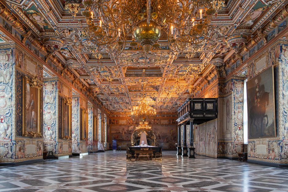 Luxurious Renaissance palace room with ornate ceilings, chandeliers, and detailed wall art.