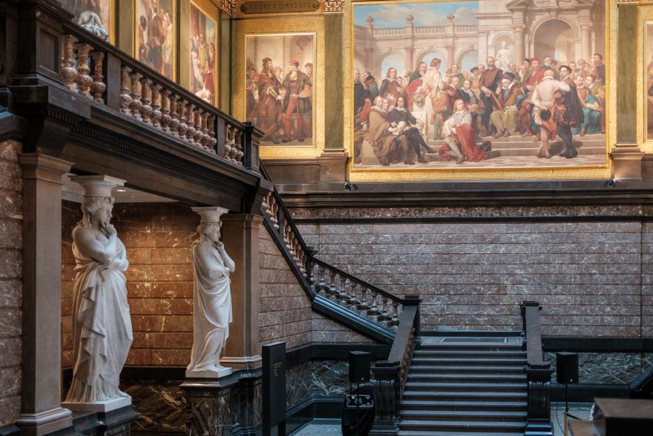 Elegant museum interior showcasing classical statues and grand staircase leading to large historical paintings.